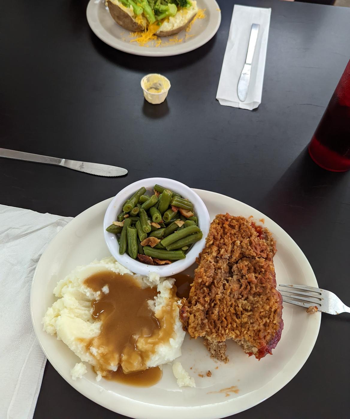 Meatloaf with mashed potatoes, brown gravy and green beans, next to a broccoli cheddar baked potato