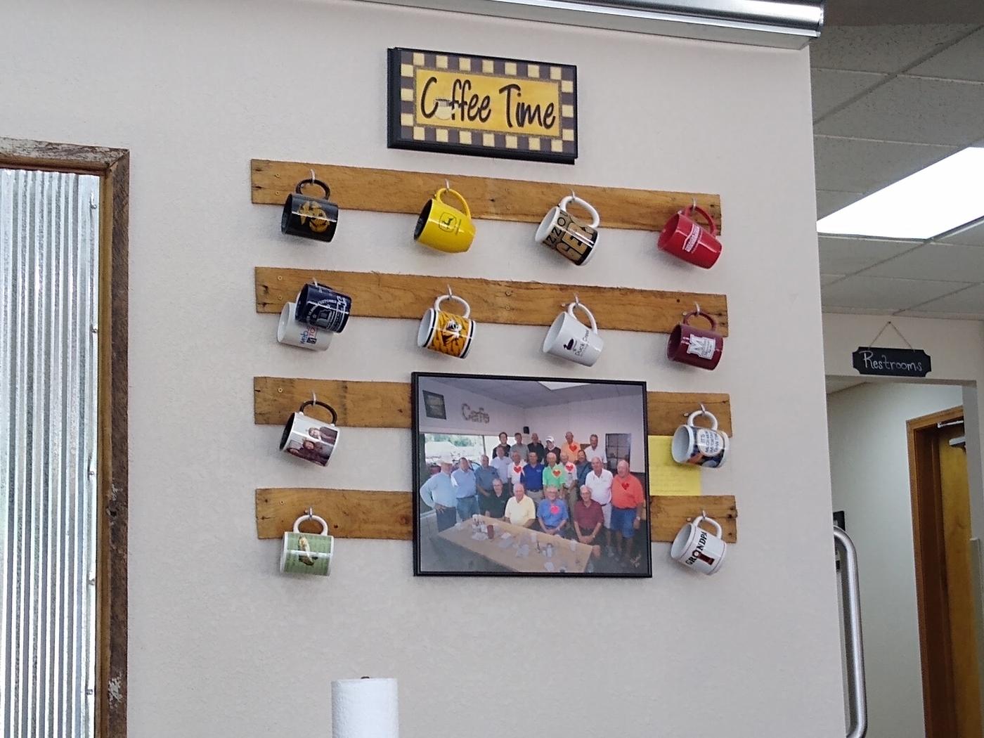 Mugs hanging on hooks from reclaimed boards under a framed Coffee Time sign
