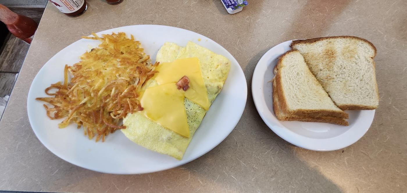 A cheese omelette with a pile of hash browns and a side plate of toast